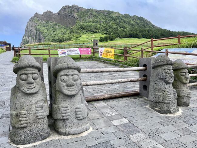 Kamenní mužíci Dol hareubang před zelenými útesy Seongsan Ilchulbong na Jeju