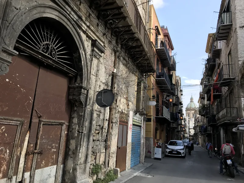 Úzká ulice historického Palerma s balkony a kupolí v dálce