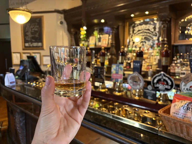 Sklenička skotské whisky před barovým pultem
